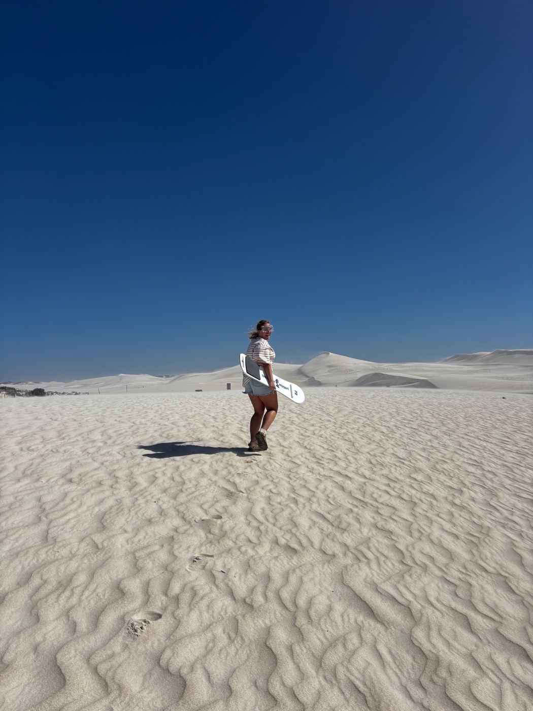 Ainsley sandboarding on white dunes, laughing